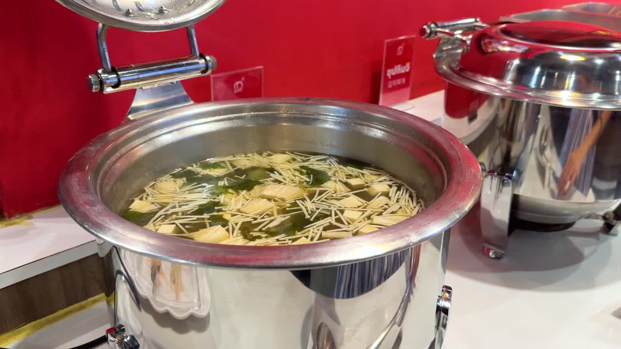 A person ladles miso soup into a bowl at a Korean BBQ buffet in Bangkok, Thailand