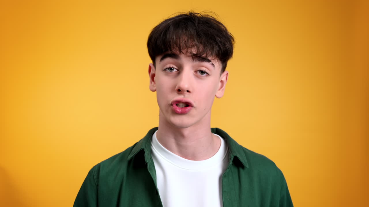 Young man talking while looking at the camera on a yellow background