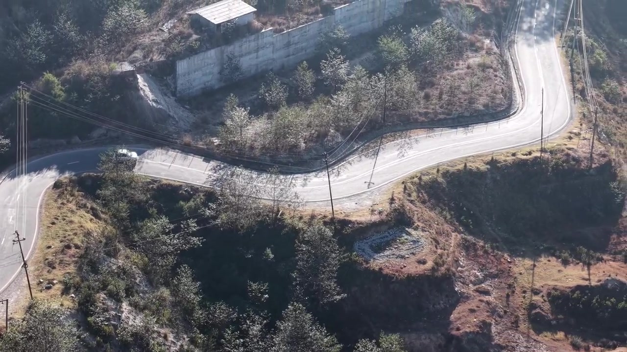 Drone perspective of a single car driving around a hairpin curve on a scenic asphalt road through forest terrain