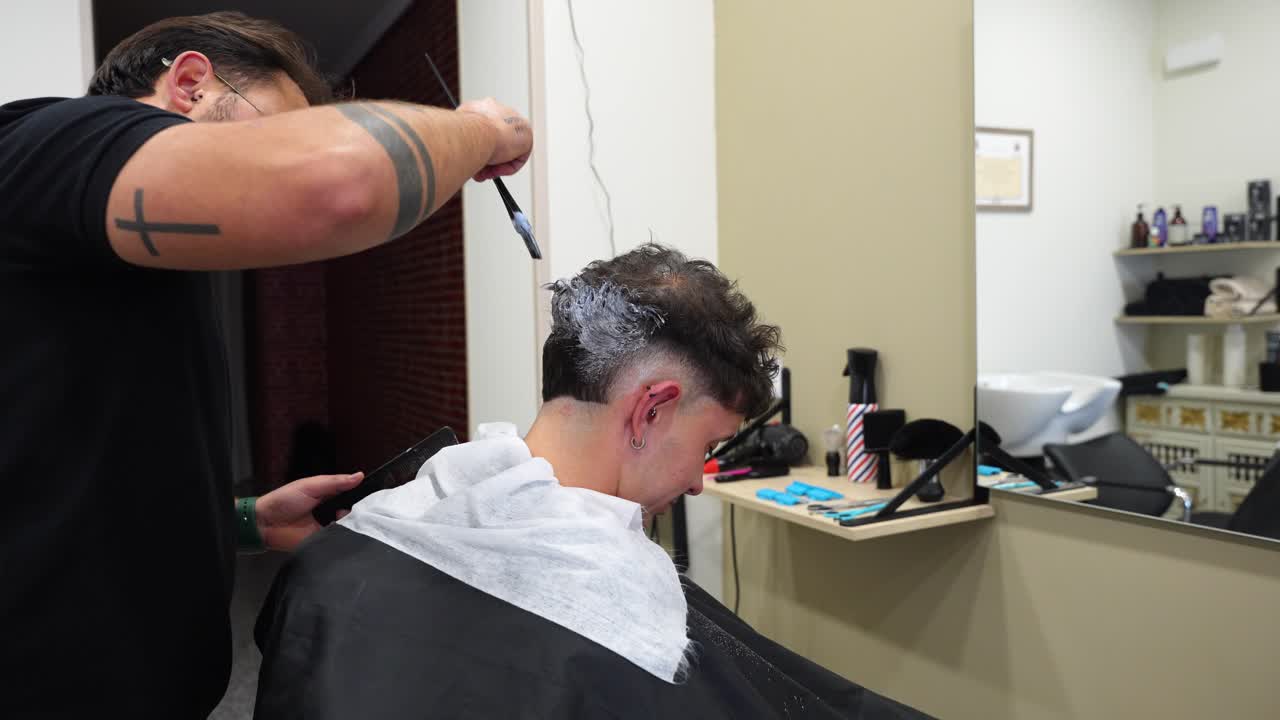 Professional barber spreads mixed bleach and oxidant cream on client’s hair to lighten tone