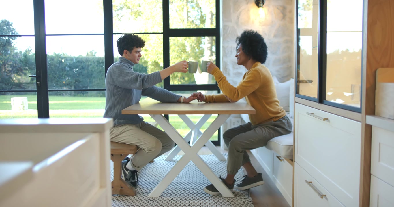African American male partners holding hands, sitting in kitchen nook, sharing coffee