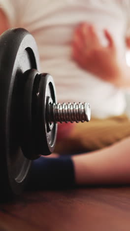 adorable little boy sits on wooden floor spinning gear on barbell with hand. curious toddler examines professional gym equipment closeup slow motion
