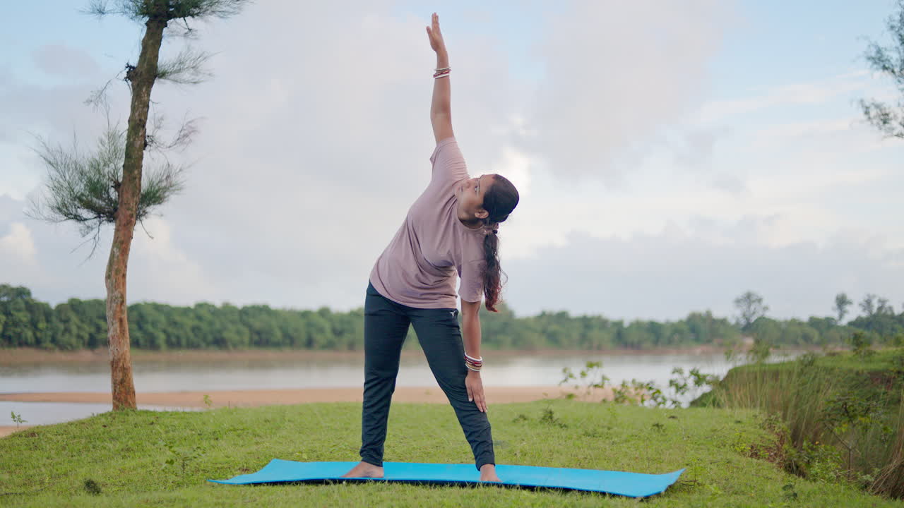 Seorang wanita melakukan pose segitiga di lingkungan alam yang tenang di pagi hari, mempromosikan kesehatan, energi yang tenang, dan penghilang stres