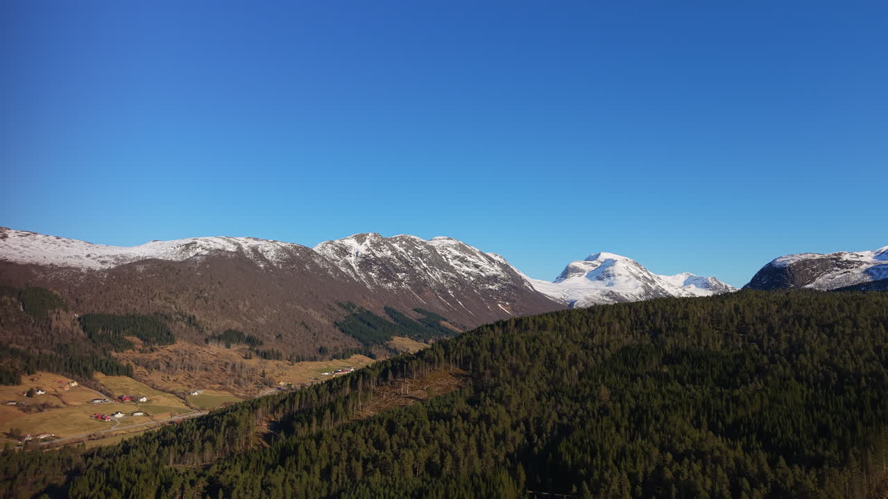 Montagne innevate dominano una vasta foresta in Norvegia. Il cielo azzurro e limpido esalta il paesaggio aspro. Ideale per documentari naturalistici o contenuti di viaggio