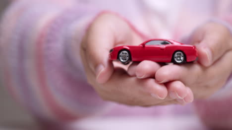 woman hand holding red toy auto represents safety in automotive investment