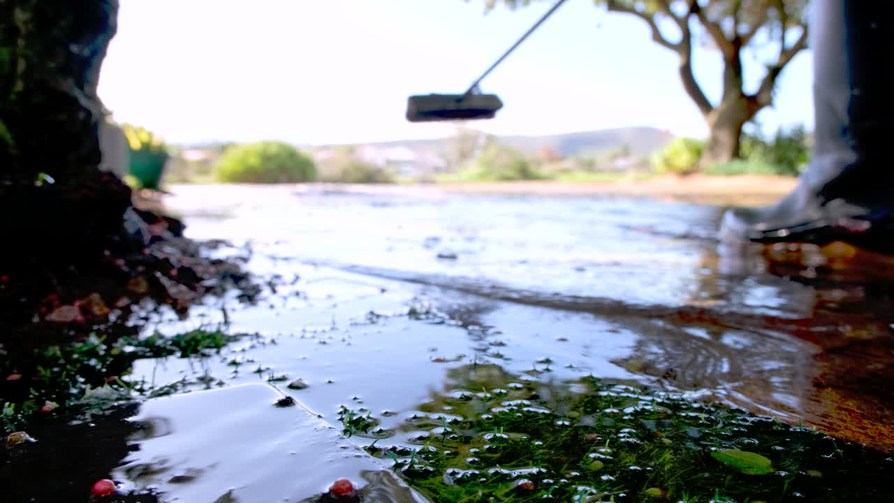 Man sweeps stormwater from heavy rain downpour off his driveway, shallow focus