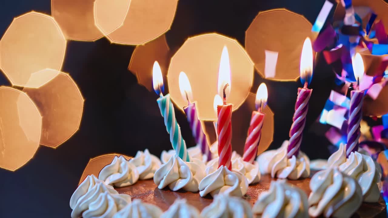 Close-up video of a birthday cake with lit candles, featuring a bokeh background