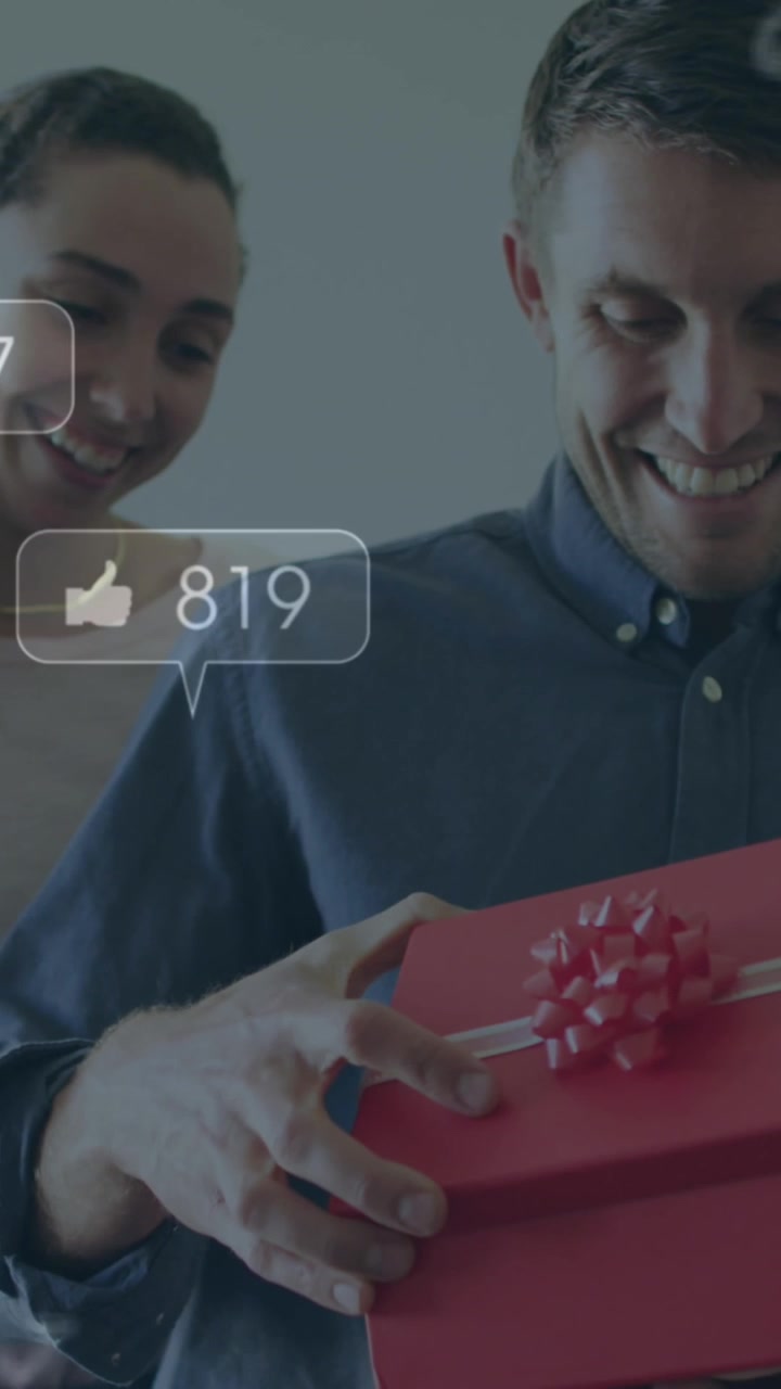 Animation of social media icons over caucasian man opening a box gifted by his home at home