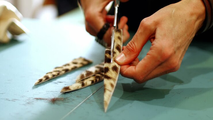 Mid-section of craftswoman cutting leather with scissors