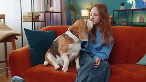 Smiling-preteen-girl-child-embracing-caressing-hugging-cute-beagle-pet-dog-sitting-on-sofa-couch