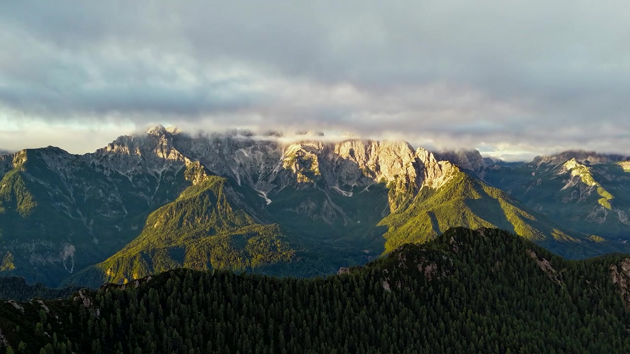 Pegunungan Alpen Julian dari Trupejevo Poldne di Karawanks, Slovenia, dengan Awan Bergerak, Puncak yang Diterangi, dan Lereng Gunung Berhutan, Selang Waktu Matahari Terbit
