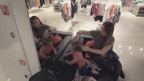 young beautiful mother with a little daughter child in a clothing store looks in the mirror mom corrects pigtails