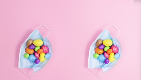 dos máscaras creativas para la cara con huevos de pascua en un fondo rosa pastel.