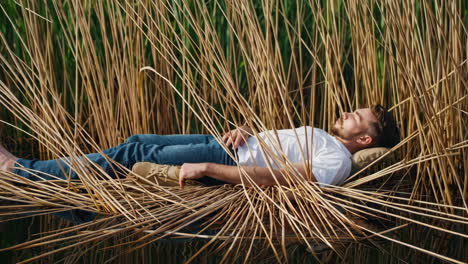 man resting peacefully in a natural reed hammock over water