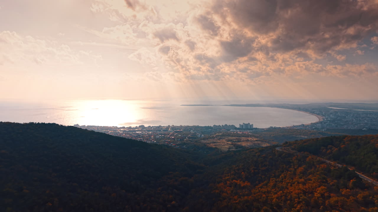 Panorama aereo di una baia marina con raggi di sole tra le nuvole. Ampia vista di una città costiera e della baia sotto un cielo drammatico con raggi solari che colpiscono la superficie dell'acqua.