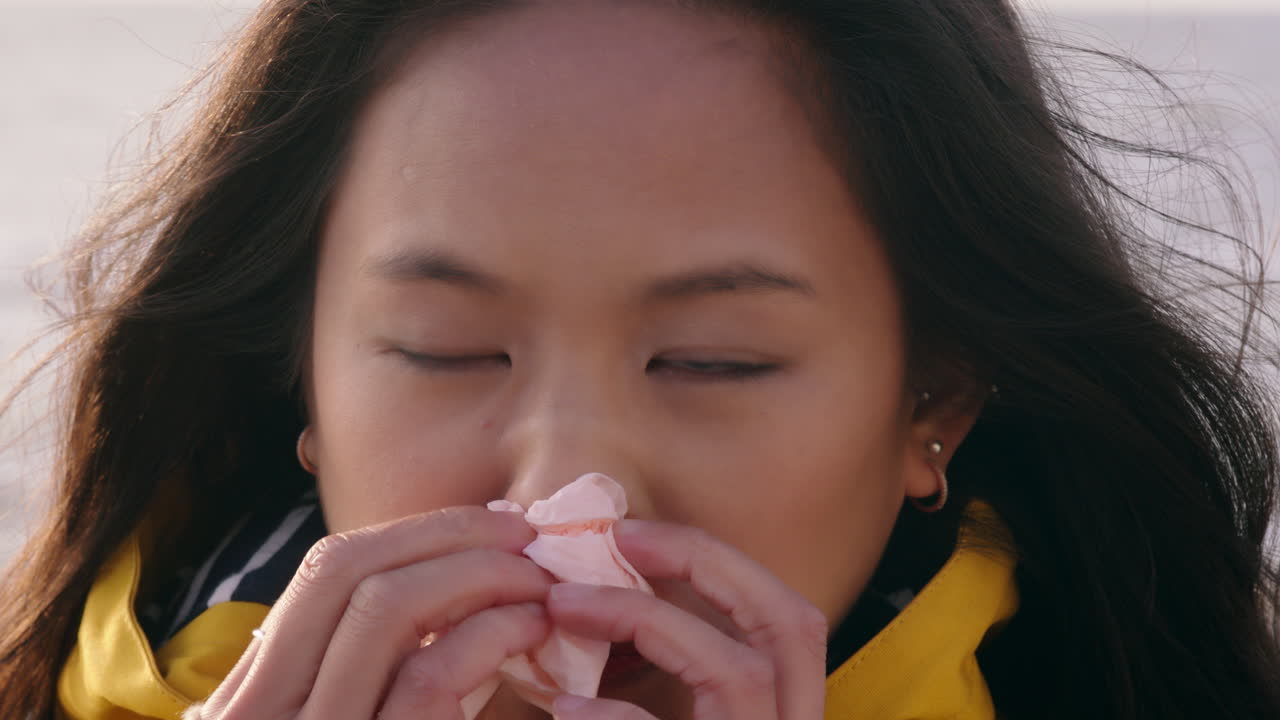 retrato de una mujer asiática enferma sonándose la nariz con un pañuelo de papel, una mujer insalubre olfateando con síntomas de gripe en la fría y ventosa playa