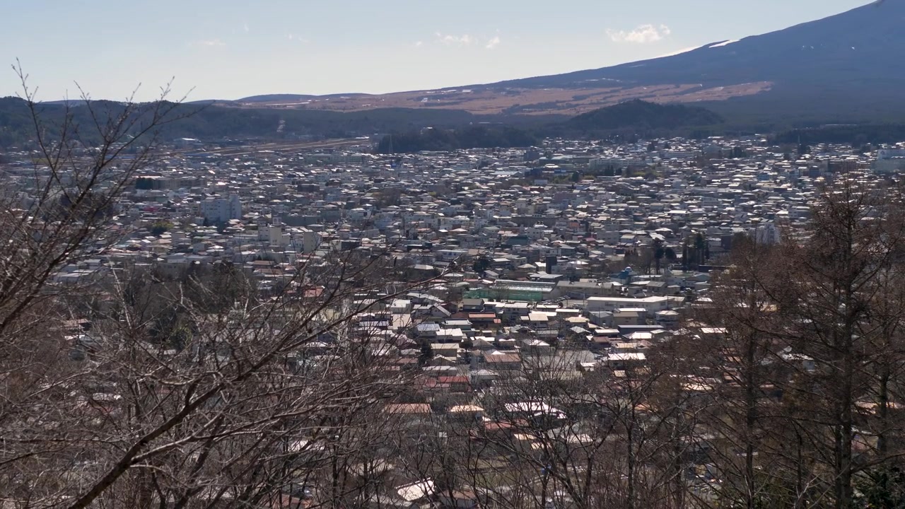 Paesaggio al rallentatore del quartiere urbano e delle abitazioni del villaggio di Fujiyoshida in una valle, con rami d'albero in primo piano, vicino al Monte Fuji nella Prefettura di Yamanashi. Turismo e infrastrutture del Giappone.
