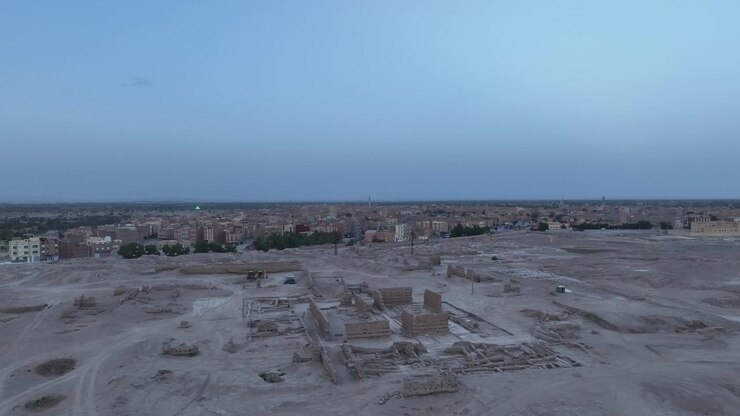 Ripresa aerea dall'alto che mostra il sito archeologico scavato dell'antica Sijilmasa con la moderna città di Rissani visibile sullo sfondo al tramonto in Marocco