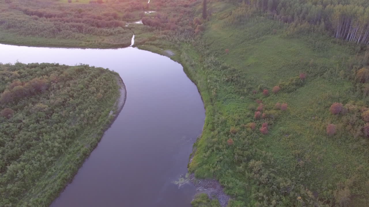 дрон наклоняется от спокойной реки к далекому закату солнца в извилистой речной долине