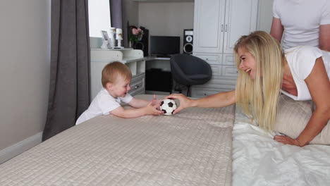 dad and mom play with the boy on the bed with the ball