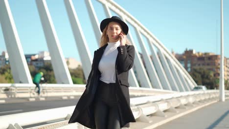 young woman talking on mobile phone on bridge in sunlight