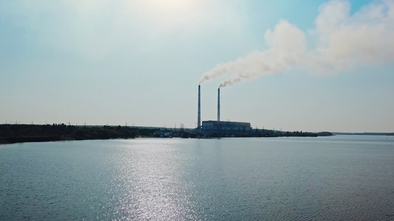 Video shot over the water in the daytime on the background of the hydroelectric power station located at the river. Camera motion top down