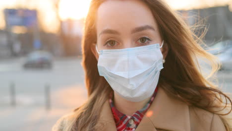 cámara alejándose de la cara de una chica triste con máscara médica parada en la calle de la ciudad y mirando la cámara