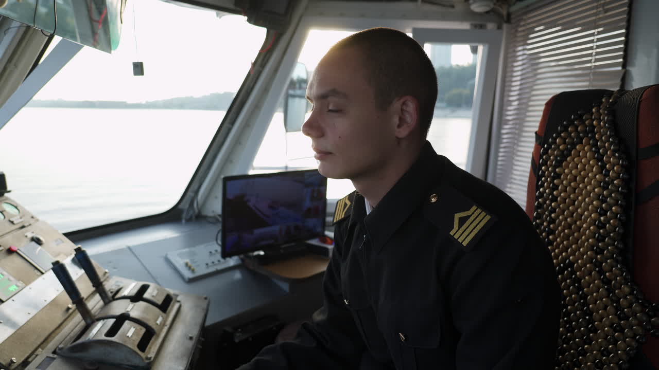 A man in uniform navigates a ship from the bridge