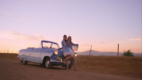 beautiful girl friends taking selfies on road trip at sunset with vintage car