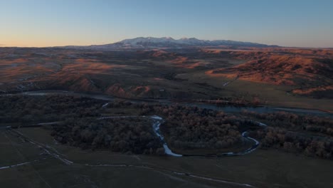 vista aérea volando hacia las montañas y un río al atardecer en montana