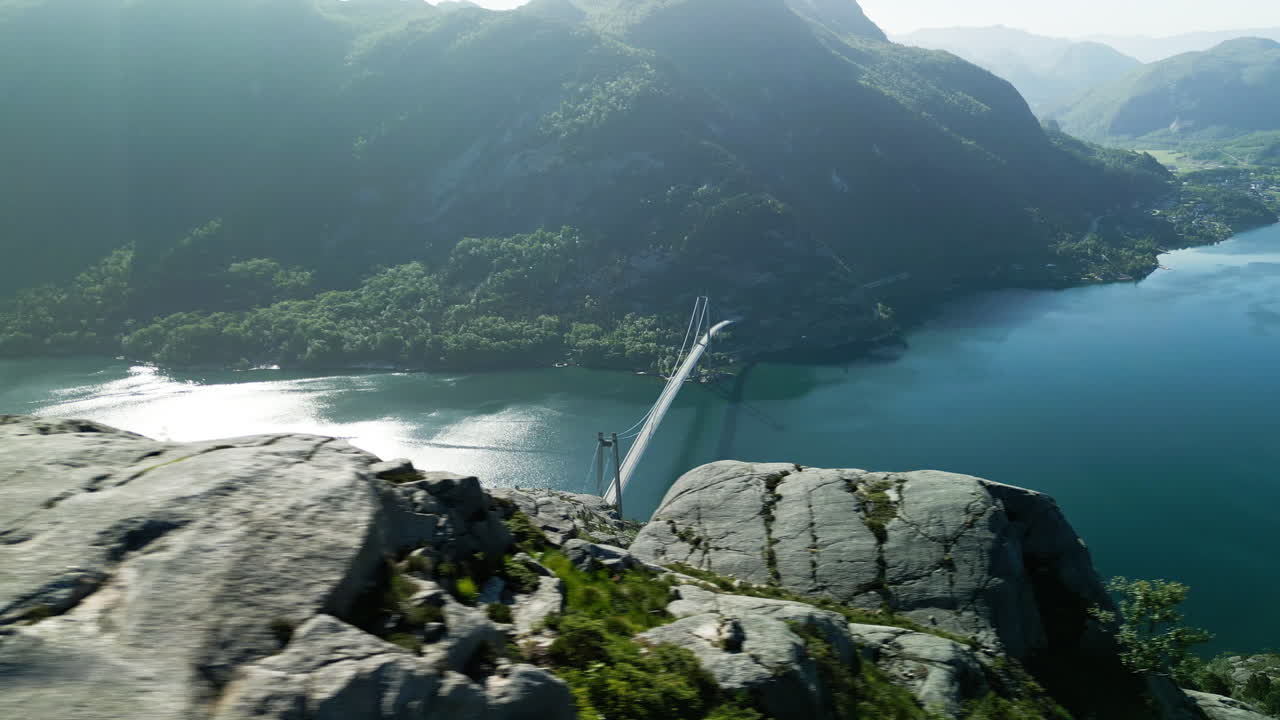 Dronebillede af Lysefjordbroen fra toppen af Sokkaknuten i Norge i solskinsvejr. Solen spejler sig i fjorden.