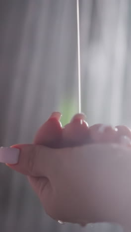 woman flows soap on hand in shower and rubs in hand. woman dispenses soap onto hand proceeding to rub in hands. water cascades around woman in shower