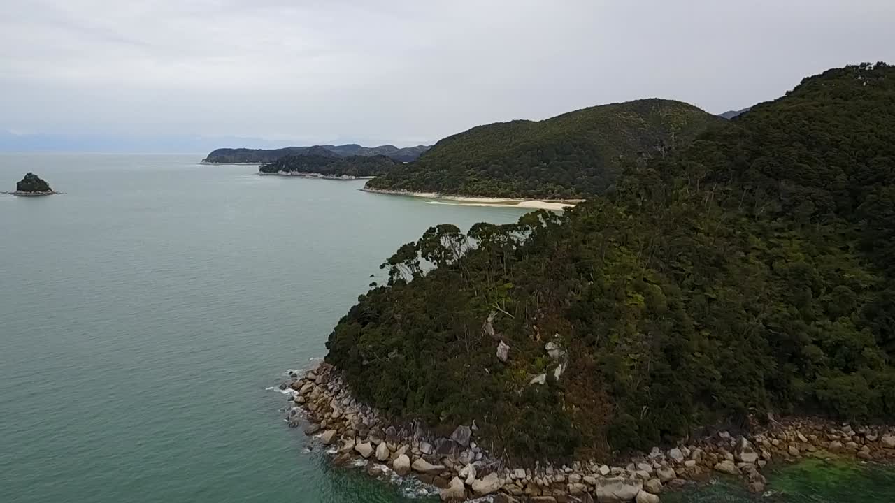 vista aérea volando sobre la playa de arena dorada y hermosas montañas verdes en el parque nacional abel tasman, nelson, nueva zelanda