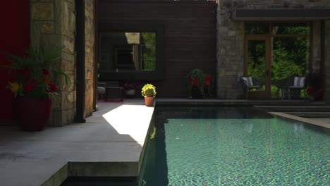 side to side movement across a long luxury blue infinity swimming pool in back yard on sunny summer day surrounding a property detailed with stone, wood and brick