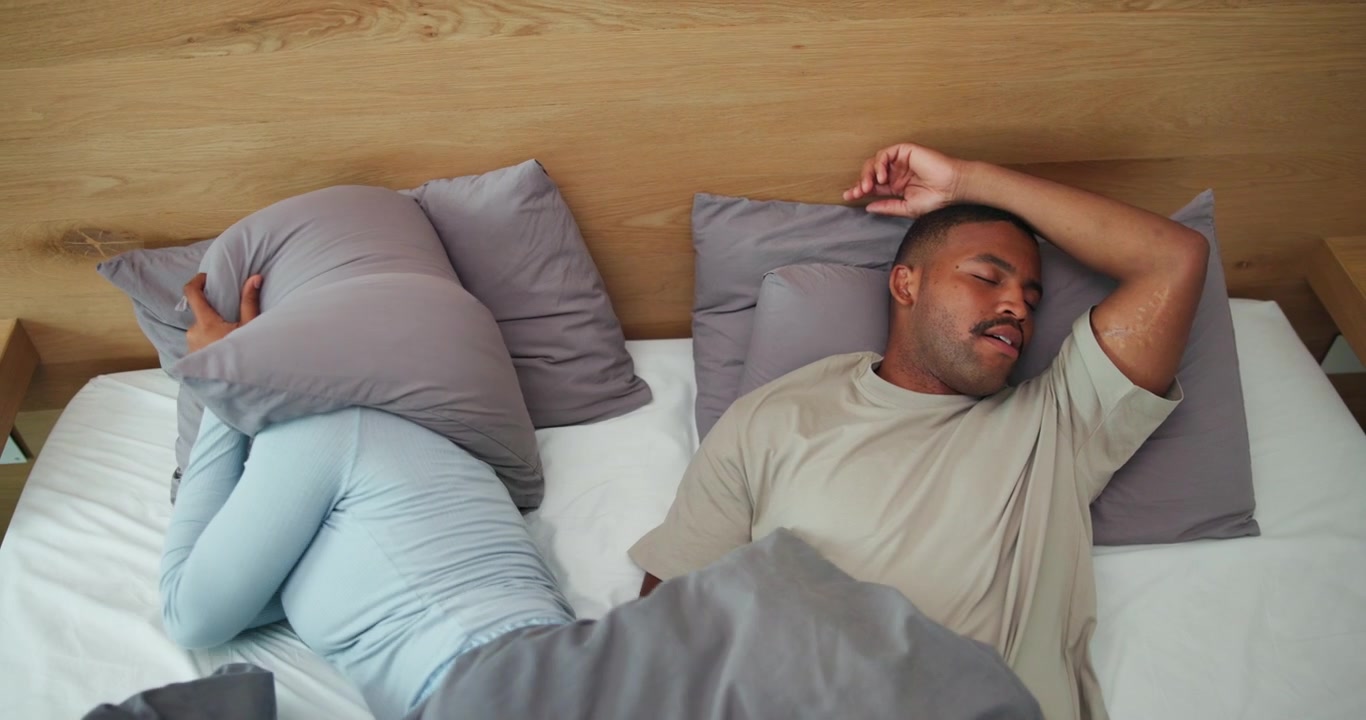 Woman Covering Her Head With Pillow While Partner Sleeps Beside Her