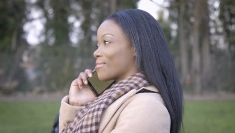 Confident-black-woman-talking-phone-in-park