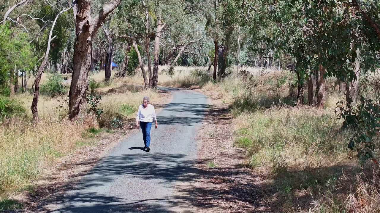 mujer mayor caminando a lo largo de una pista de bicicletas y bicicletas al lado del lago mulwala, nsw, australia
