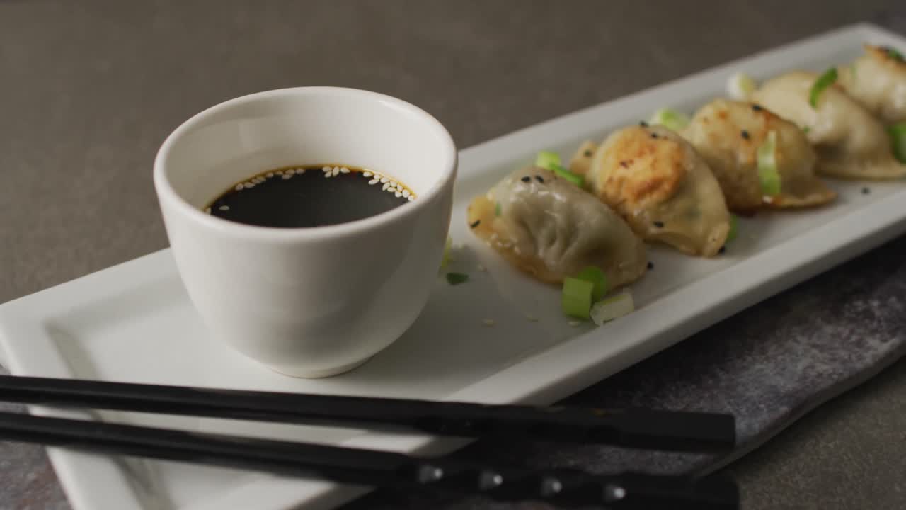 Composition of plate with gyoza dumplings and soy sauce with chopsticks on grey background