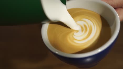 professional female barista makes rosetta in cappuccino - close up