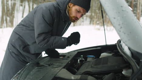 man stuck in the winter forest holding a torch and checking his car engine problem 1