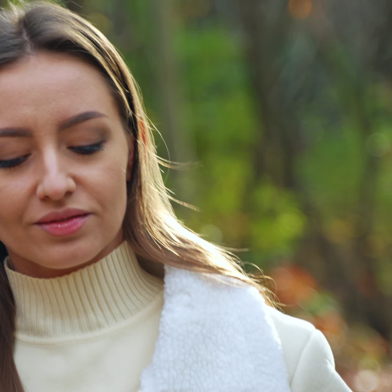 Beautiful romantic girl with long straight hair walks by the autumn park. Lady enjoys the rays of sun and coffee from a paper cup