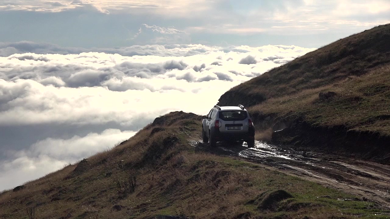 SUV su strada di montagna fangosa sopra le nuvole