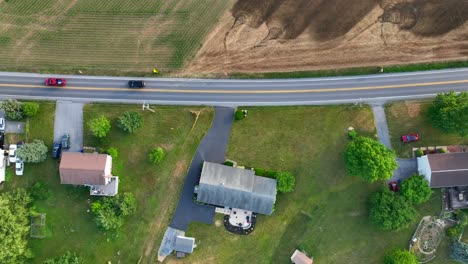 Top-down-aerial-truck-shot-of-cars-on-street-with-field-on-one-side-and-houses-on-the-other