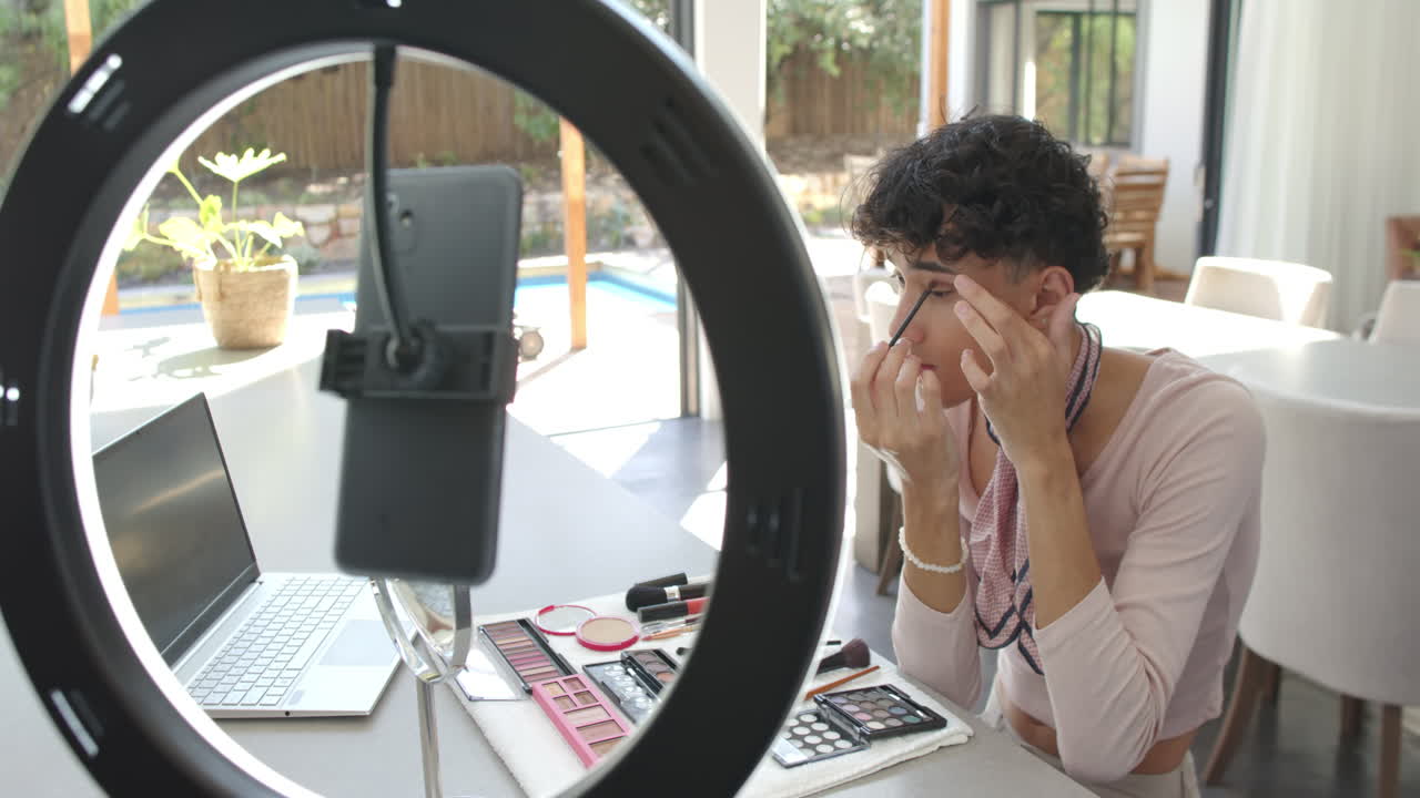 Applying makeup, non binary person recording video with smartphone and ring light