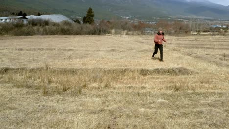 young woman chasing after dog running through remote field in chinese mountains