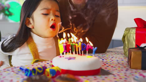 Familie-Mit-Zwei-Vätern-Feiert-Zu-Hause-Den-Geburtstag-Ihrer-Tochter-Und-Bläst-Kerzen-Auf-Kuchen-Aus