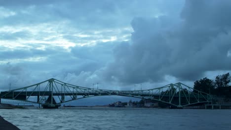 Time-lapse-of-beautiful-fast-moving-dark-gray-rain-clouds-over-the-Oskara-Kalpaka-swing-bridge-in-Liepaja-city-in-evening,-wide-shot