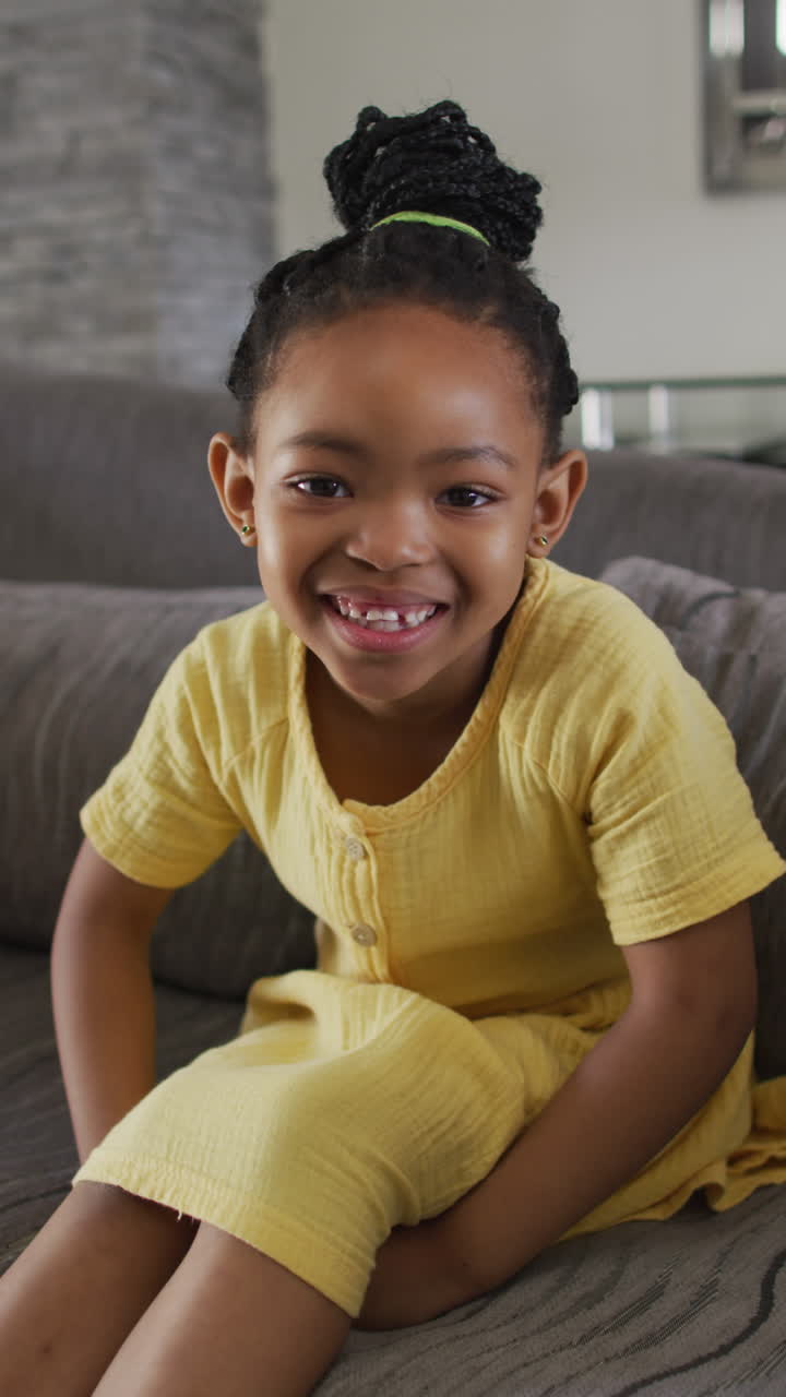 retrato vertical de una chica afroamericana sonriente sentada en el sofá en la sala de estar