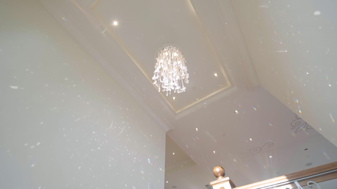 럭셔리한 가정집의 우아한 샹들리에가 햇빛을 굴절시켜 아름다운 별빛 효과를 만들어내는 넓은 시네마틱 샷이에요