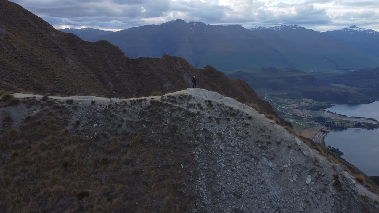 Young caucasian woman running and looking around on a path along a mountain ridge to a viewpoint at Roy's Peak, Wanaka, New Zealand.